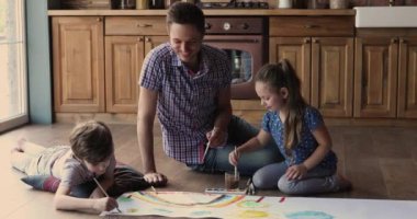 Baba ve küçük çocuklar kağıt çarşafa boyayla resim yaparlar.