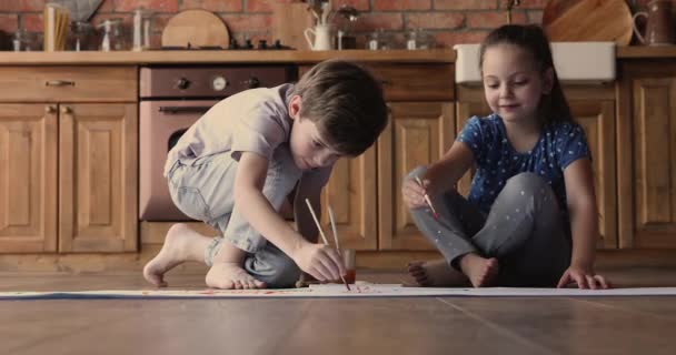 Los niños se sientan en el suelo pintando sobre papel con pinturas — Vídeo de stock