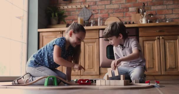 Os irmãos brincam em casa com ferrovias de brinquedo e blocos de madeira — Vídeo de Stock