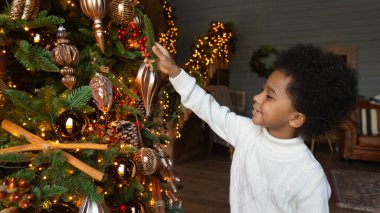 Gülümseyen Afrikalı Amerikalı çocuk Noel süsleri asıyor.