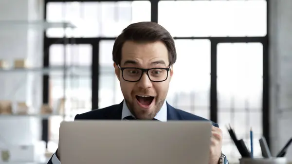 Overgelukkig jonge zakenman in bril op zoek naar laptop scherm. — Stockfoto