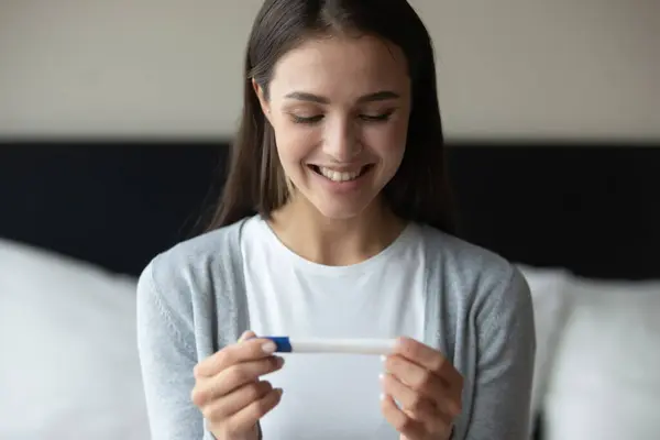 Izgalmas Y-generációs nő, aki a terhességi teszt pozitív eredményét tanulmányozza — Stock Fotó