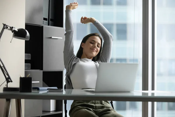 Happy millennial female stretching with pleasure sitting at office table — Stock Photo, Image
