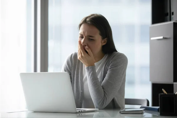 Немотивированная женщина не может устоять перед зевотой сидя за ноутбуком в офисе — стоковое фото