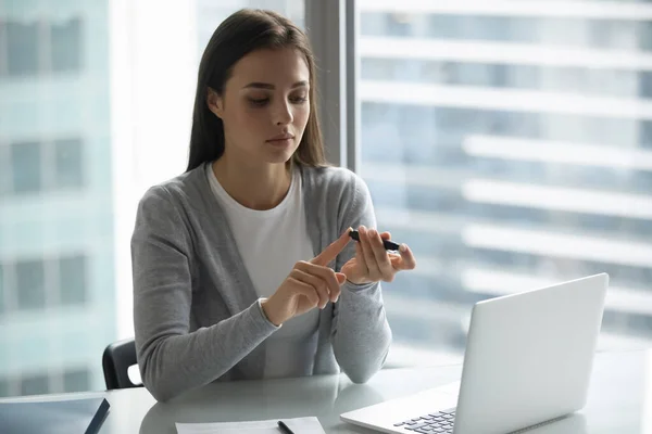 Travailleuse de bureau millénaire utilisant un glucomètre électronique sur le lieu de travail — Photo