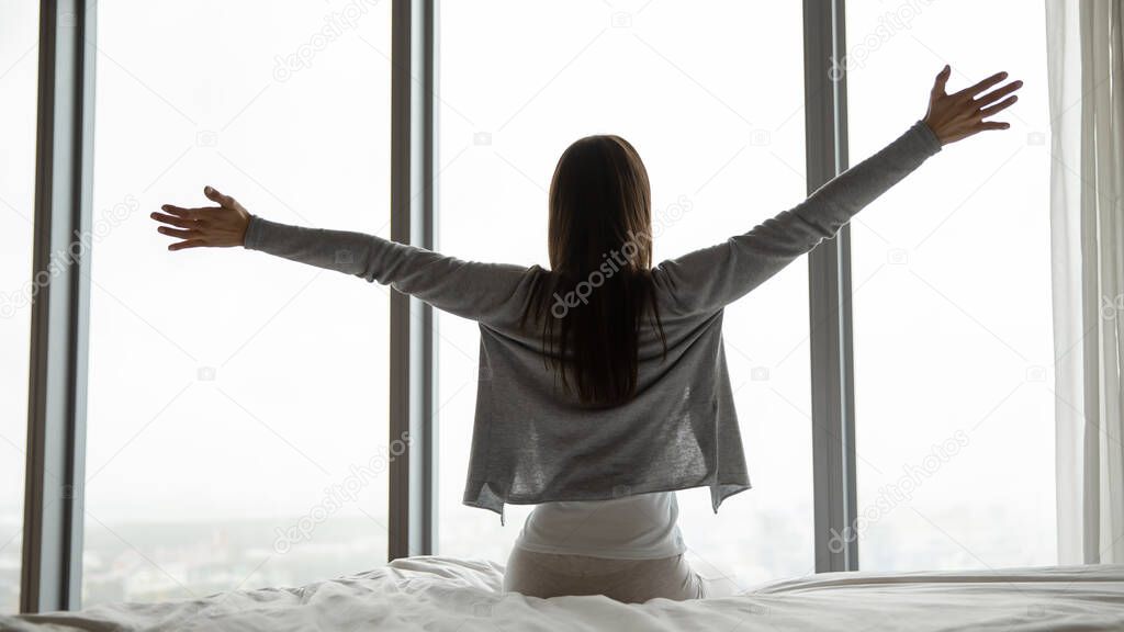 Rear view of woman sitting on bed in comfortable room