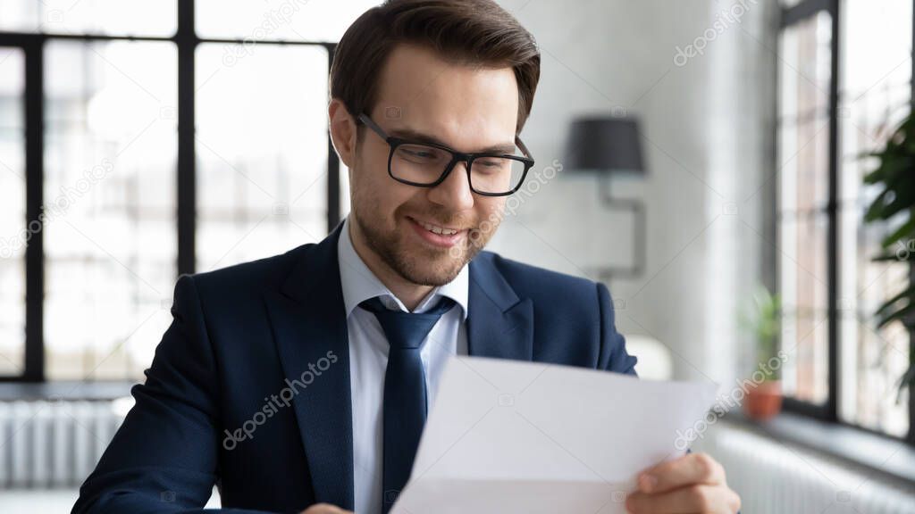 Smiling young executive manager reading pleasant news in correspondence.