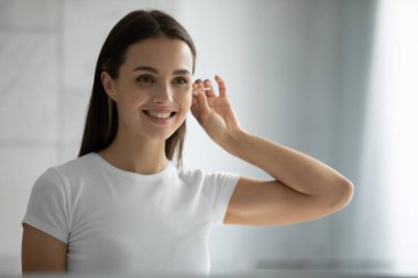 Hoş bir genç kadın banyoda dikilip aynanın kulaklarını temizliyor.