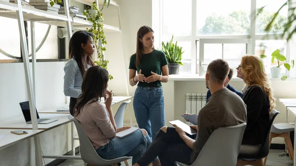 Confident young lady trainer gives recommendations to diverse employee group — Stock Photo, Image