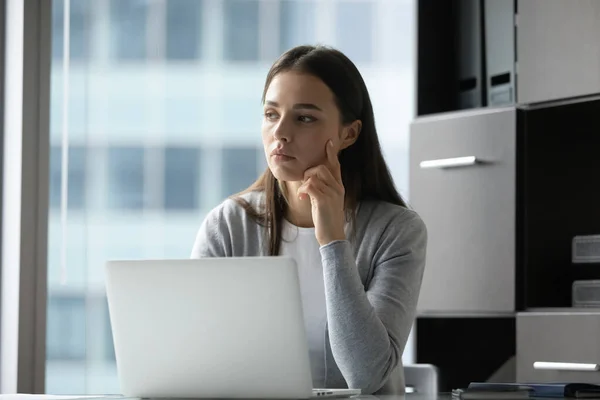 Pensativa empleada milenaria sentada en el portátil distraída del trabajo — Foto de Stock