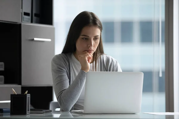 Pensive female sitting at office desk looking at laptop screen — Stock Photo, Image