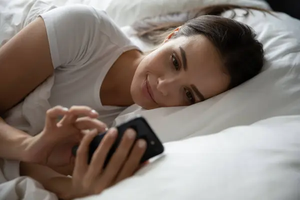 Tinédzser lány feküdt az ágyban mobiltelefonnal elalvás előtt — Stock Fotó