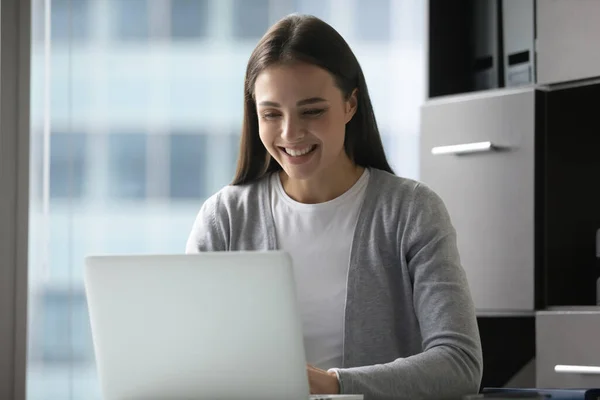 Travailleuse souriante assise dans un bureau tapant un message sur un ordinateur portable — Photo