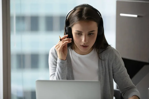 Attentive female student sitting in headphones by laptop studying online — Stock Photo, Image