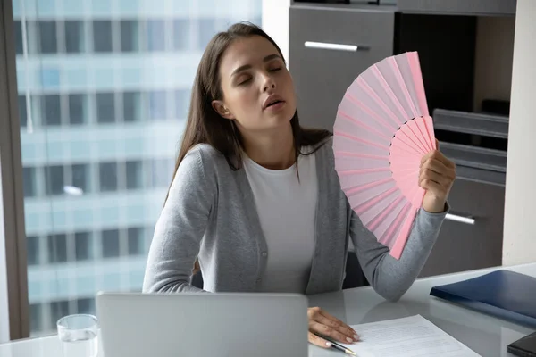 Exhausted female office worker waving herself with hand fan