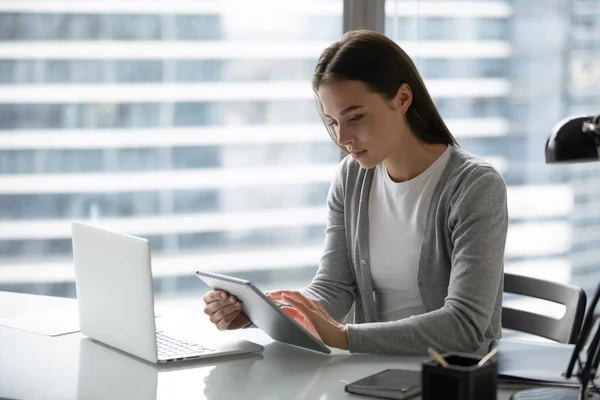 Concentrated young businesswoman synchronizing data at pad and laptop memory — Stock Photo, Image