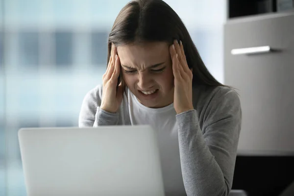 Нервная офисная работница обнимает голову в панике перед ноутбуком — стоковое фото
