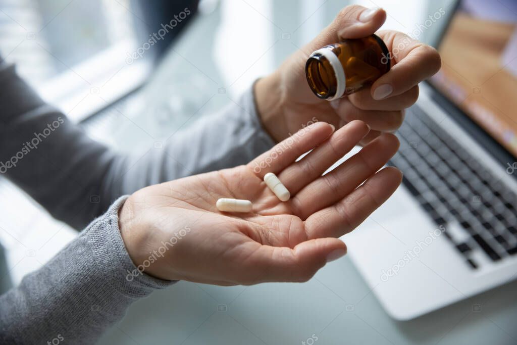 Millennial lady taking pills at workplace to relief of pain