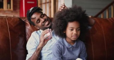 Afrikalı şefkatli bir baba küçük kızları tarıyor. Kıvırcık saçları var.