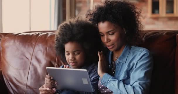 Liten flicka sitta med mamma på soffan användning tablett enhet — Stockvideo