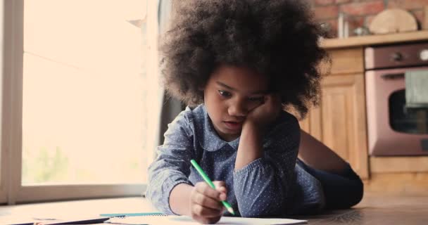 Chica africana acostada en el suelo dibujar en cuaderno de bocetos en la cocina — Vídeos de Stock