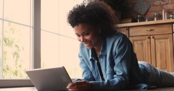 Hermosa mujer africana acostada en el suelo de la cocina con dispositivo de tableta — Vídeos de Stock