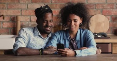 Afrikalı çift mutfakta oturuyor ve akıllı telefon kullanıyor.