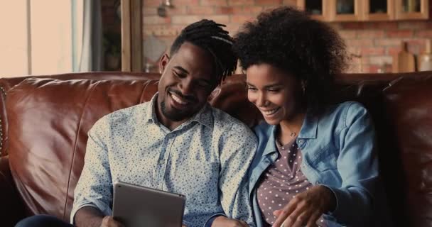 African couple relaxing on couch using tablet wireless gadget — Stock Video