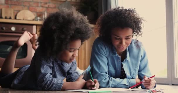 부엌 바닥에 누워 있는 아프리카 가족이 스케치 책에 그림을 그리는 모습 — 비디오