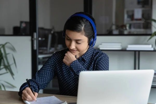 Zelfverzekerde Indiase zakenvrouw het dragen van koptelefoon briefjes schrijven, met behulp van laptop — Stockfoto