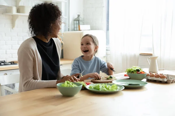 興奮した白人の女の子とともにアフリカ系アメリカ人の母親調理サラダ — ストック写真