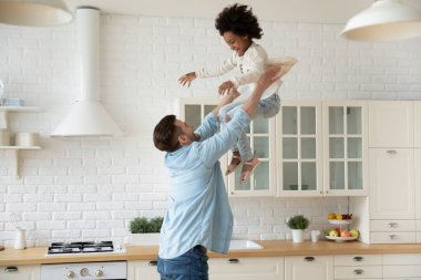 Heyecanlı genç baba küçük Afrikalı Amerikalı kızı havaya fırlatıyor.