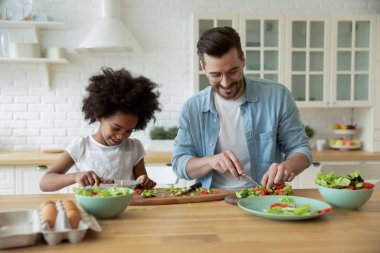 Genç baba ve Afrikalı Amerikalı kız birlikte yemek pişiriyorlar.