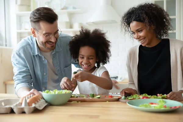 Glückliche Eltern mit kleiner Tochter, die gemeinsam Salat kochen — Stockfoto