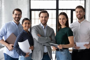 Kendine güvenen erkek takım lideri, çeşitli çalışanlarla birlikte resim için poz veriyor.