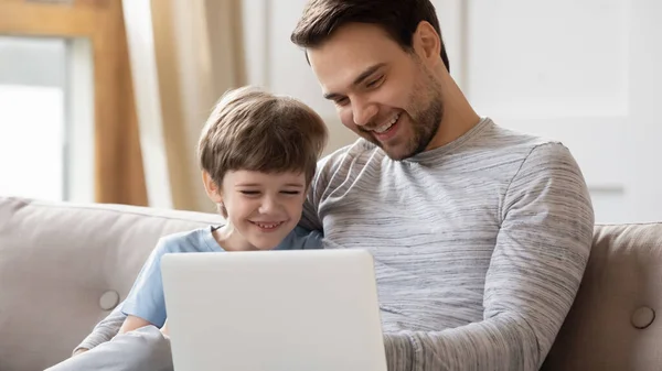 用笔记本电脑把快乐的年轻父亲和可爱的儿子紧紧拥抱在一起 — 图库照片