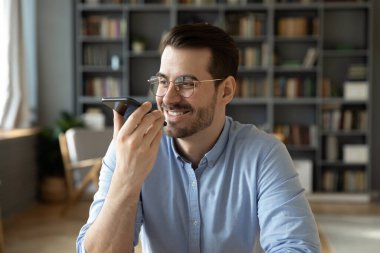 Gülümseyen işadamı elinde akıllı telefonla ofiste oturuyor. Sesli mesaj bırakıyor.