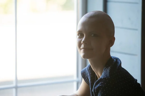 Mujer joven sonriente tranquila que recibe tratamiento contra el cáncer sentada por la ventana —  Fotos de Stock