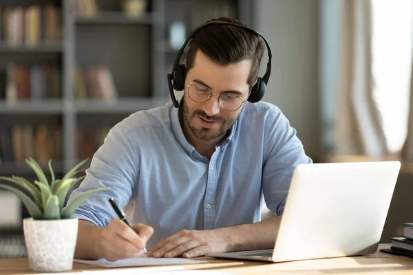 Hombre usar auriculares ver webinar utilizando notas de escritura portátil —  Fotos de Stock