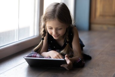 Gülümseyen küçük kız yerde dijital ped kullanarak yatıyor.