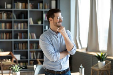 Kendine güvenen mutlu iş adamı modern ofiste duruyor ve düşünüyor.