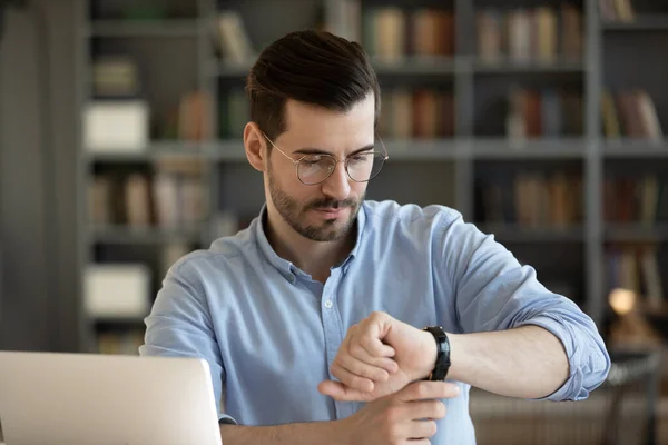 Hombre de negocios mira el reloj de pulsera comprueba el tiempo en el lugar de trabajo — Foto de Stock