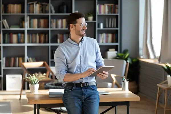 Entrepreneur holding tablet device looks out the window feels happy