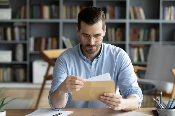 Serious businessman sit at desk holding envelope take out letter — Stock Photo, Image