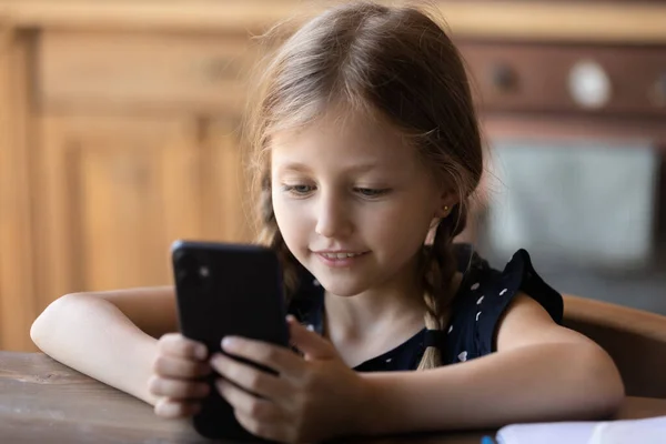 Smiling little girl sitting at home making videocall by smartphone — Stock Photo, Image