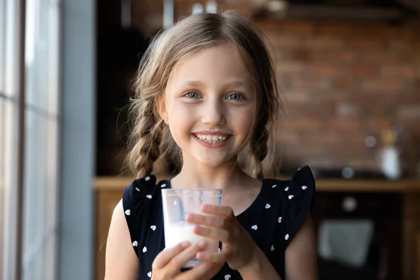 Niña alegre con bigote de leche sosteniendo un vaso de yogur — Foto de Stock