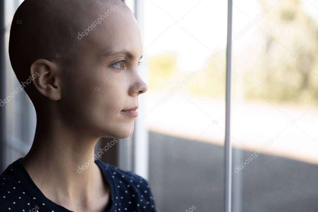 Concentrated young woman receiving cancer treatment standing close to window