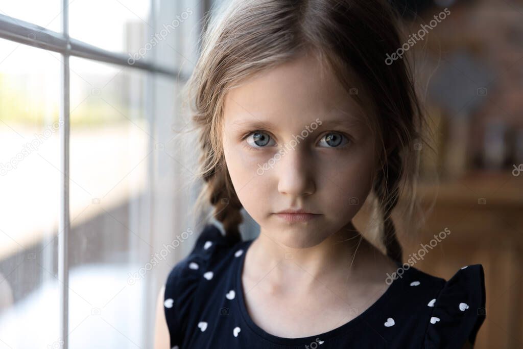 Portrait of serious little school age girl standing by window