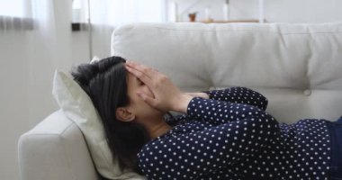 Üzgün ağlayan genç Asyalı melez kadın kanepede yatıyor..