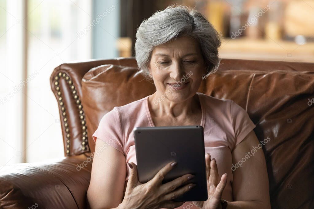 Close up smiling mature woman using tablet, having fun online